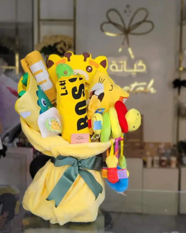 بوكيه مولود من كياتة — ألعاب وملابس أطفال صفراء ملفوفة في بطانية صفراء بشريطة خضراء